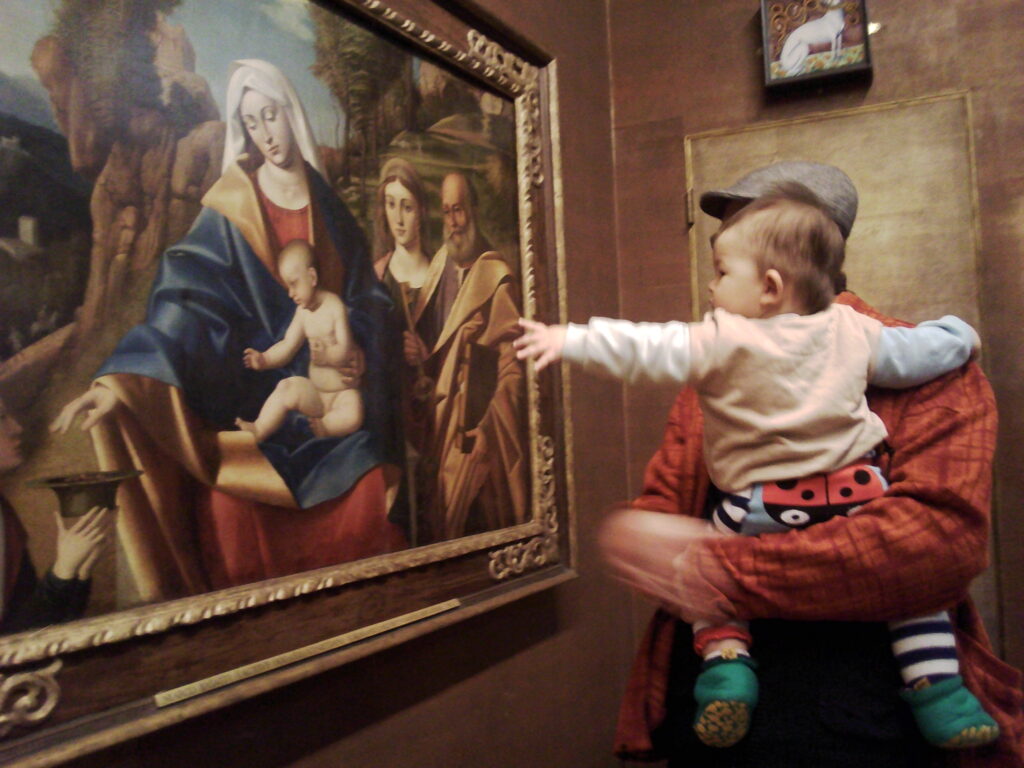A parent and young child looking at a painting together, the child pointing at the painting.