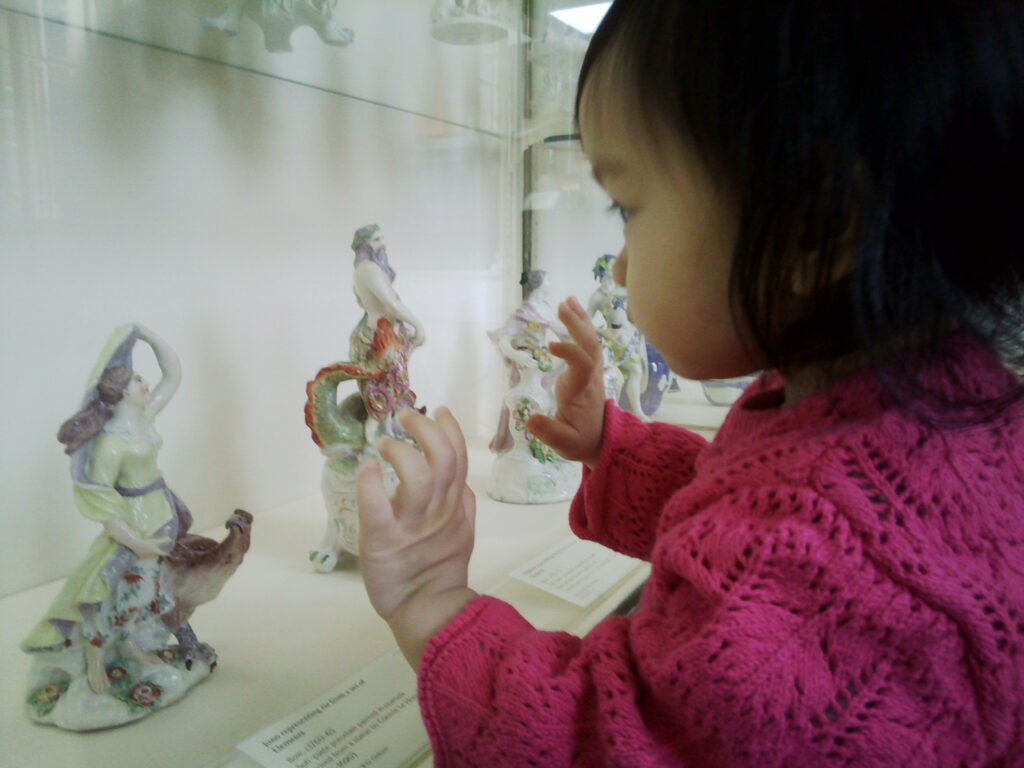 A young child looking intently at ceramic figures in a glass case.