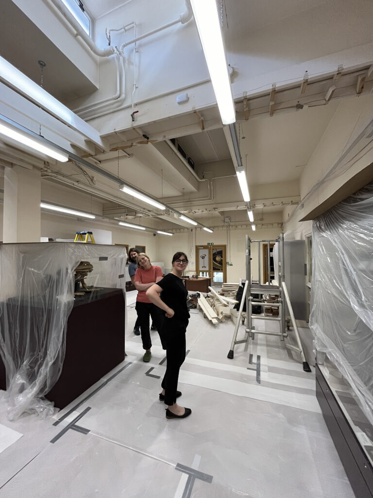 Three members of the museum team stand in the Learning Gallery which has been emptied and the remaining objects covered in plastic sheeting in preparation for the removal of the ceiling.