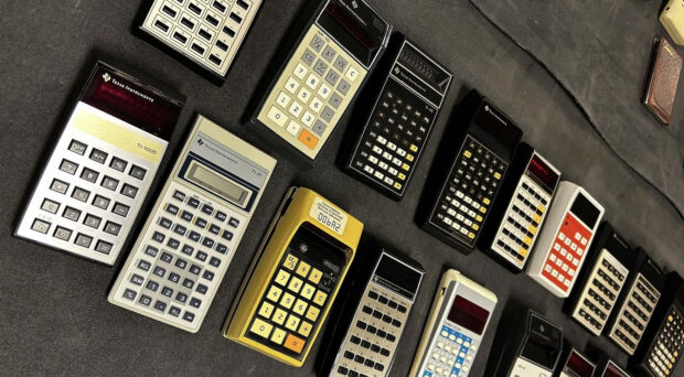 A collection of calculators lined across a table with a black tablecloth.