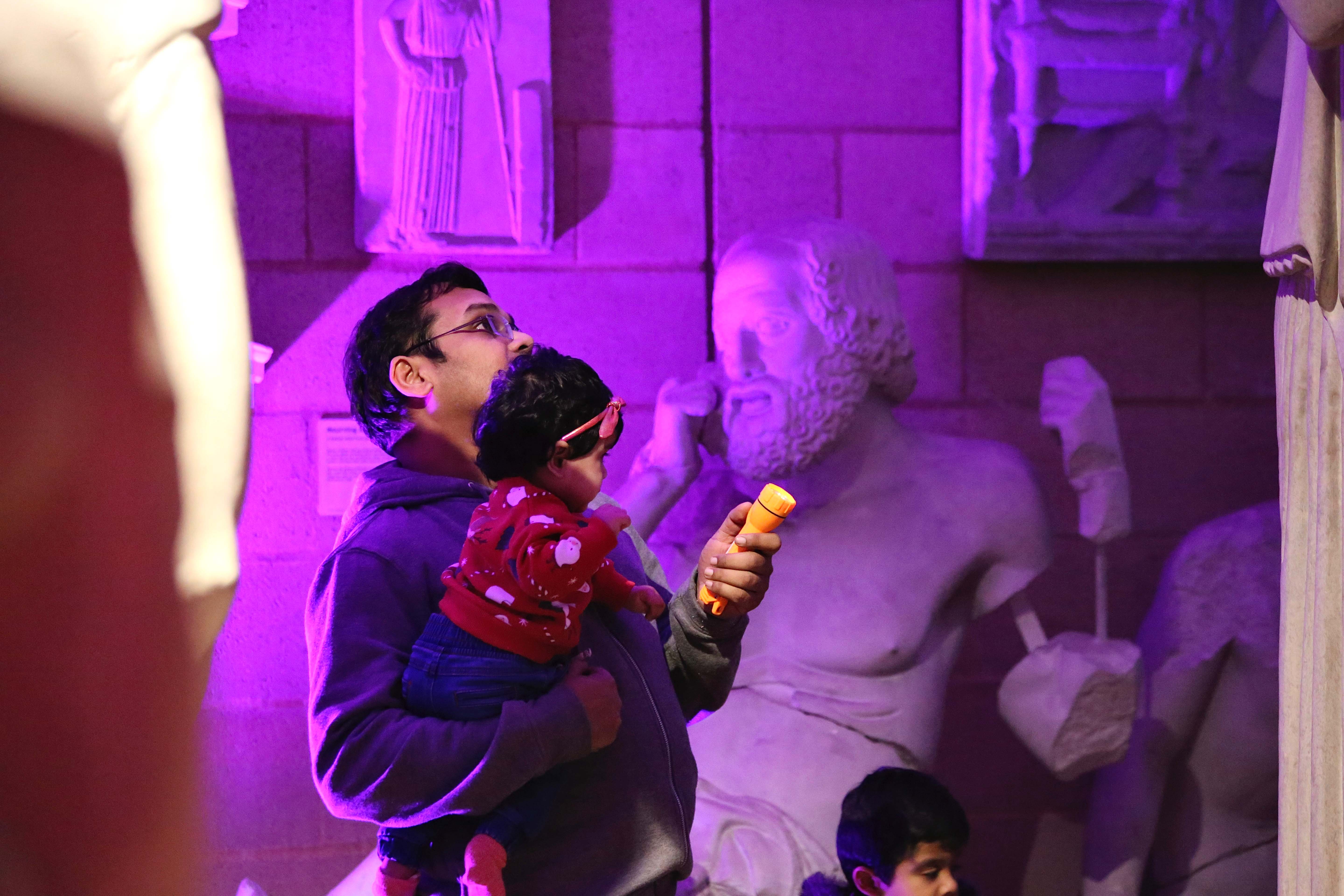 A father and child looking at a statue in a colourfully lit museum