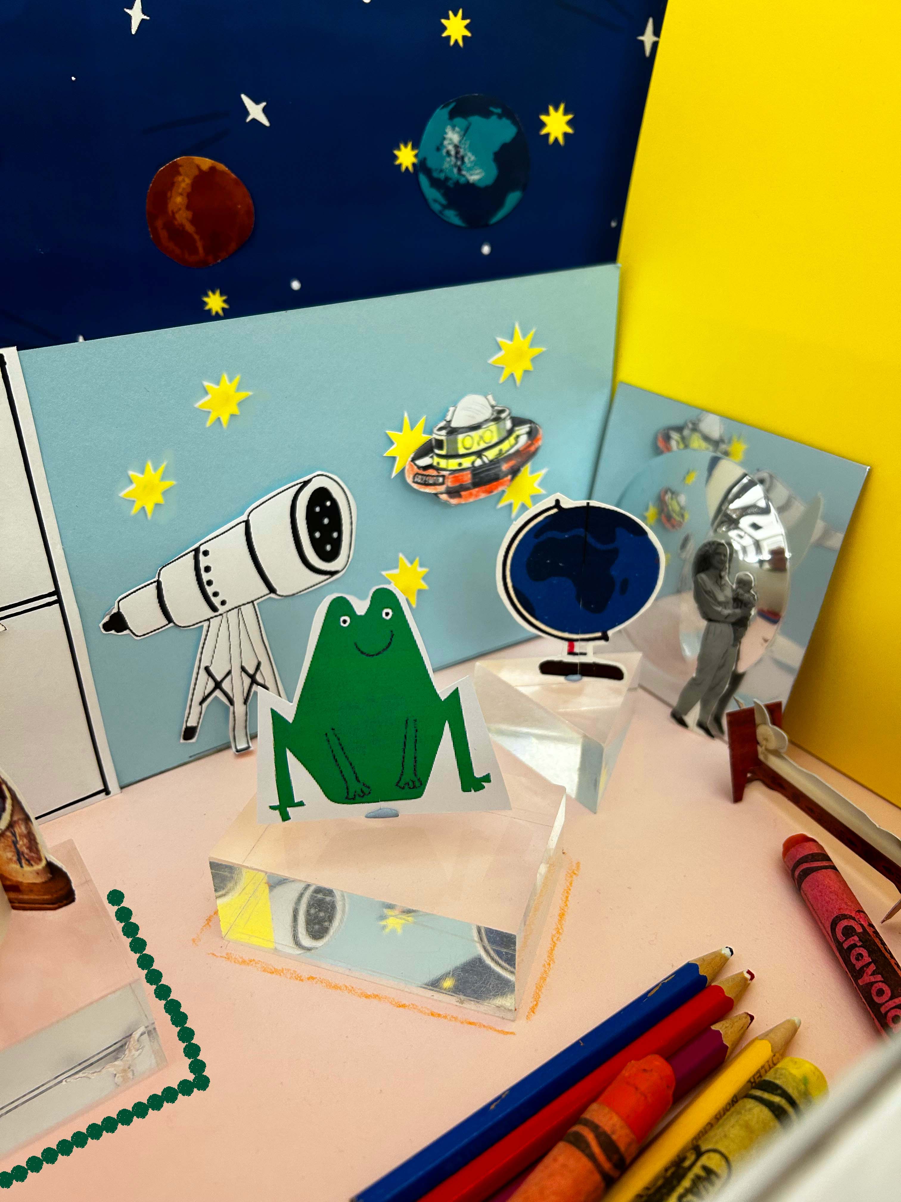 A mini model of a museum, for a educational family activity. Showing a model frog, the solar system, a globe and craft supplies.