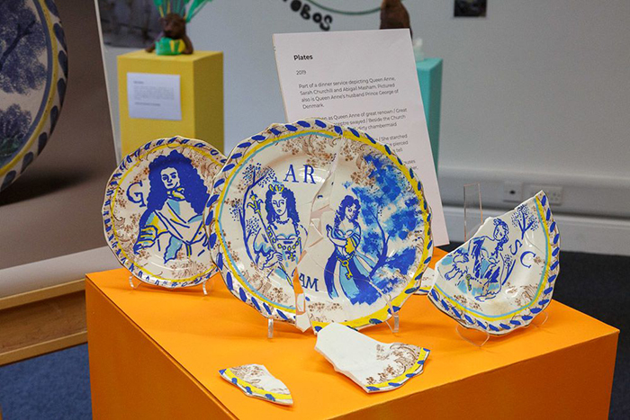 A display of plates, reassembled using tape, depicting Queen Anne and her lovers