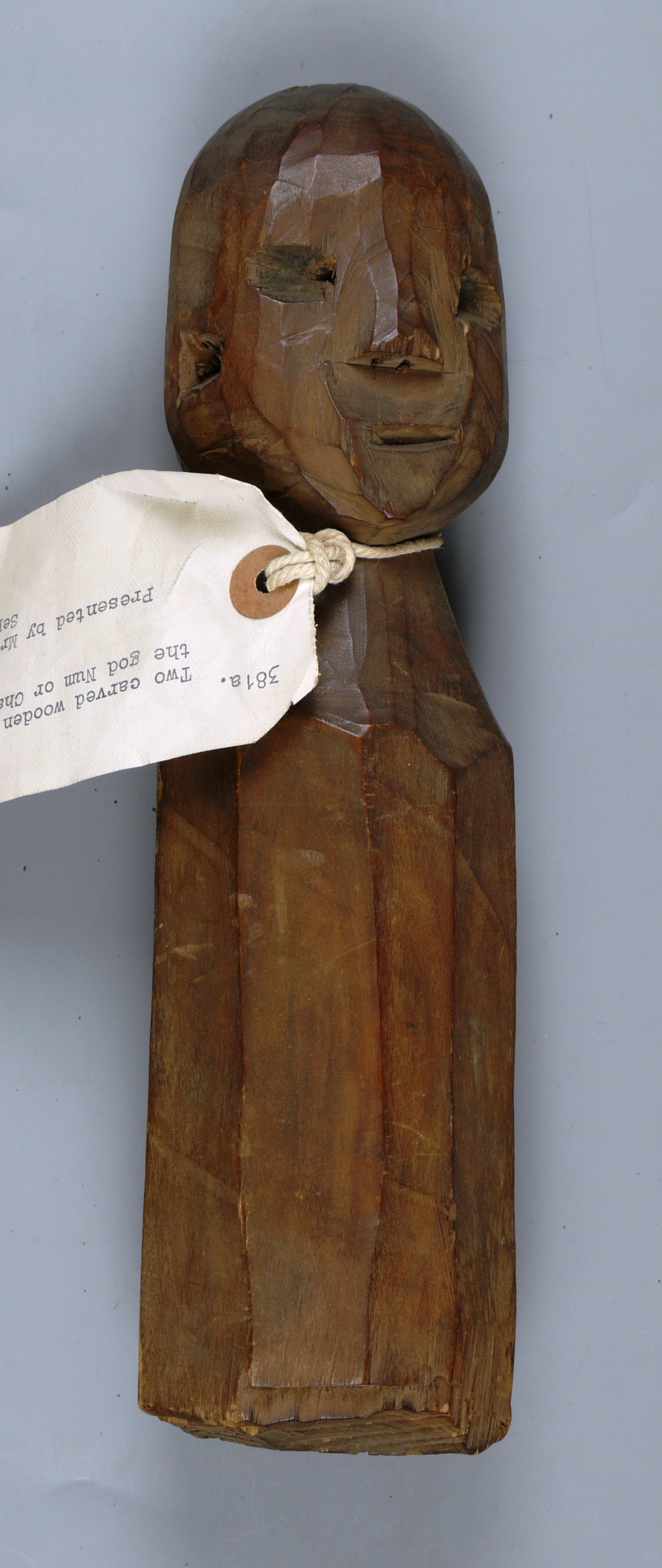 carved, human figure made of wood with a label tied around its neck