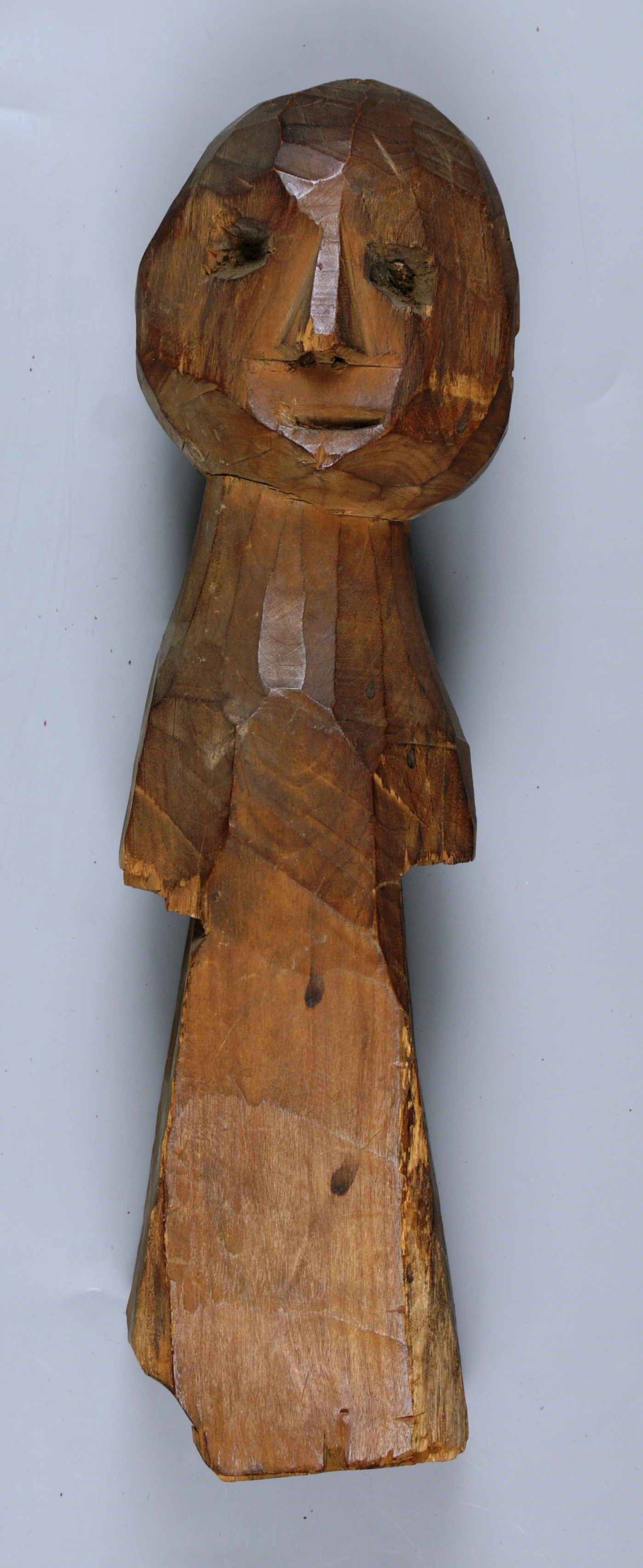 carved, human figure made of wood: shaped with a head and face and a torso. the surface of the wood is shiny