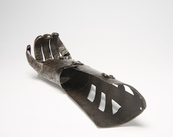 iron prosthetic hand, viewed down the armpiece towards the wrist as it lies with the palm up. The fingers and thumb curl upwards. Two fasteners are visible half way up the arm and at the wrist.