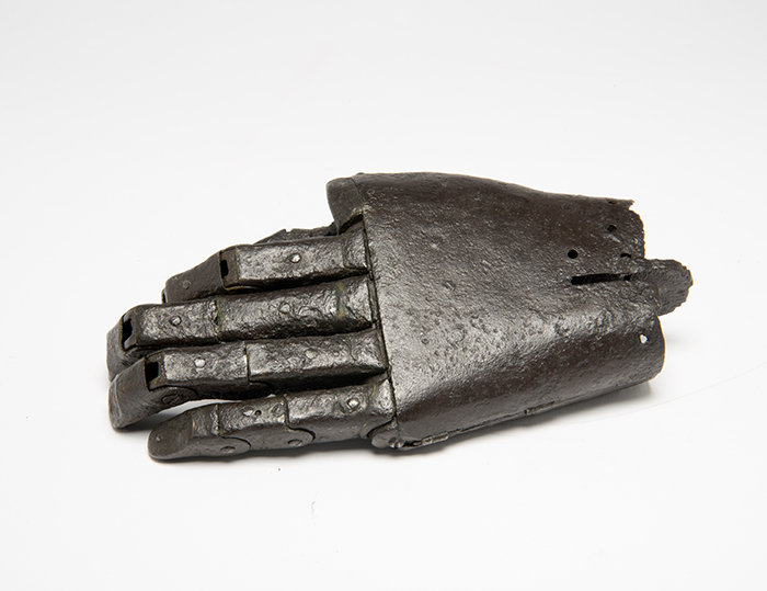 iron prosthetic hand top view, showing the back of the hand and fingers. The back of the hand is flat and smooth, with a notch at the wrist end where it would have been attached. 
