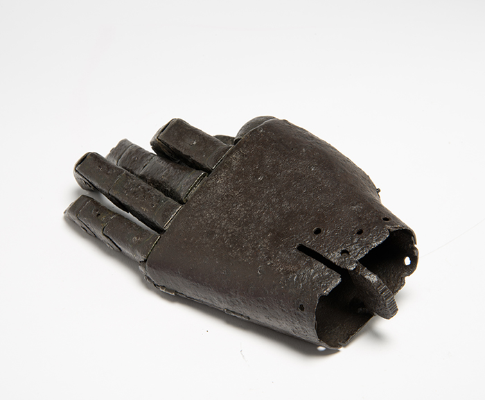 iron prosthetic hand viewed from the wrist, showing the hollow inside. The wrist is rather narrow and not cushioned. Also visible along the left hand side of the hand are hinges.