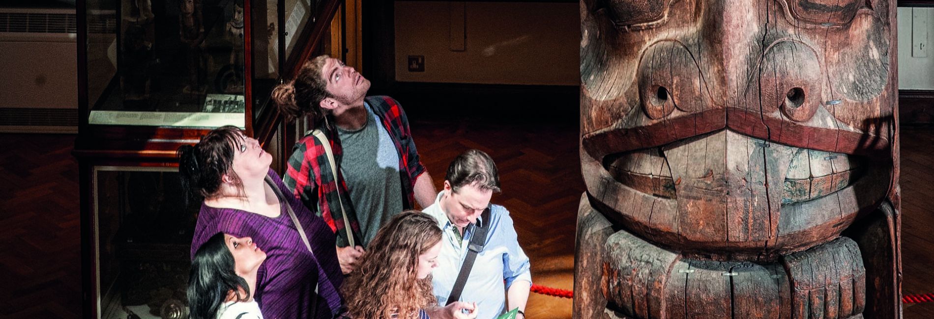 five people looking at a totem pole in the Museum of Archaeology and Anthropology