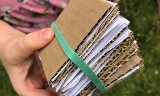 Image of child's hand holding a mini flower press made out of cardboard 