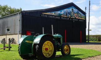 Green tractor sitting outside large barn