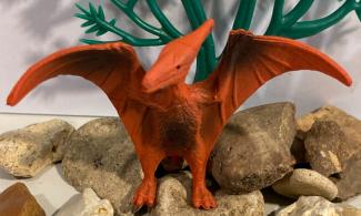 Orange model of a pterodactyl standing on stones in front of plastic greenery