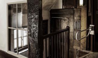 Detailed image of part of an old wooden landing showing part of a staircase, wooden panelling, timber frames and a window