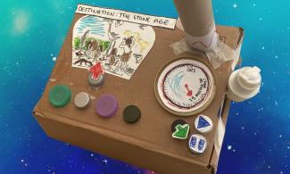 Cardboard box decorated with coloured plastic dials and a picture of 'To the Stone Age'