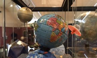 A globe with a model of sputnik on one side and a flying saucer on the other 
