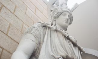 View looking up at the head of a large statue of the goddess Athena, wearing an elaborate helmet.
