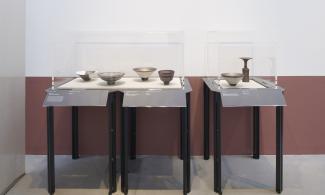 A photo of two glass exhibition cases from Lucie Rie: The Adventure of Pottery containing pots in varying colours and designs.
