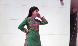 Photo of a woman in a green dress with pink, orange and yellow embroidery. Polaroid, 1973, from the archive of Inaash Al-Mukhayim. Courtesy of INAASH.