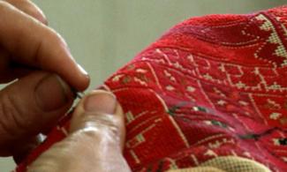 A hand holding a piece of embroidered cloth as the other hand embroiders it.