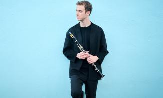 A man against a blue wall holding a clarinet