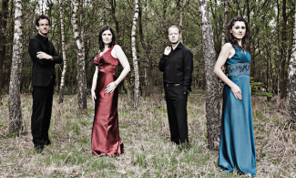 Four people in formal dress stood in a wooded area