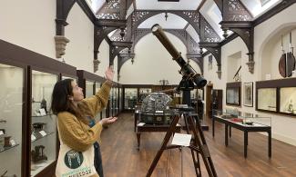 A girl holding her hands up looking looking at a telescope in the Whipple Museum