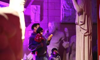 Man with two children looking up with a torch at a statue. 