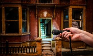 Hand holding torch shines a light into a dolls house