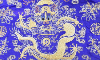 Detail from a blue silk robe decorated with a. goldwork dragon curled around a flaming pearl.