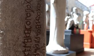 View of a museum gallery with a close-up of a writing on the side of a statue.