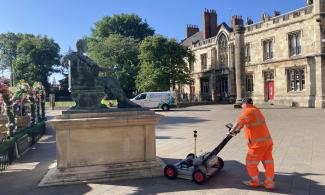 A man wearing orange hi-vis and pushing equipment next to a statue.