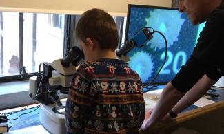 A child looking down a microscope, and a star-shaped fossil on the screen attached to the microscope.