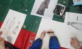 Images of children's hands as they draw a statue. 