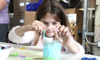 Young girl gluing coloured tissue paper to a glass jar