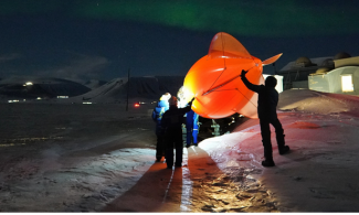 A group of scientists inflate a balloon on Arctic ice, at night
