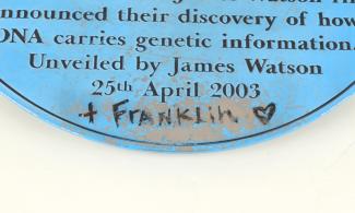 blue plaque with text about Crick and Watson and graffiti "plus Franklin" and a heart