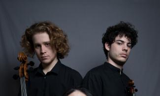 Three people sit together holding a cello