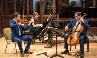 Three people sit on chairs in a concert hall, playing their musical instruments.