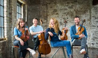 Four people sat on chairs smiling, holding musical instruments.