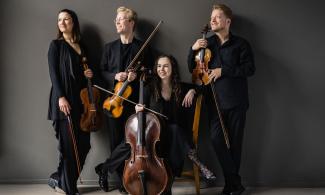 Four people stand holding their musical instruments, leaning against a grey background.