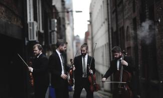 Four men standing in an alley between two buildings, holding musical instruments.