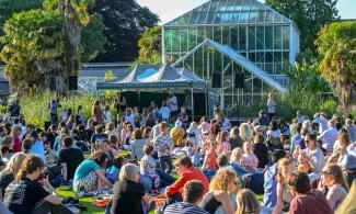 Groups of people sit in front of the marquee with a band playing music in the Garden.