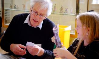 An older man and young girl sitting at a table building a "pop up museum" from paper