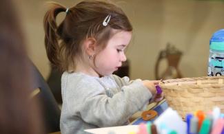 alt= "a young girl with brown hair plays with arts and crafts supplies"