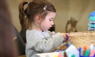 alt= "a young girl with long brown hair tied in a ponytail plays with arts and crafts supplies"