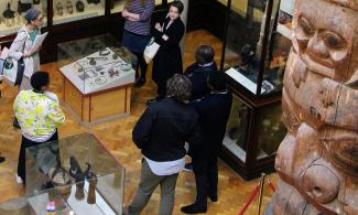 A group of men and woman listen to a talk standing in a gallery at the Museum of Archaeology and Anthropology.