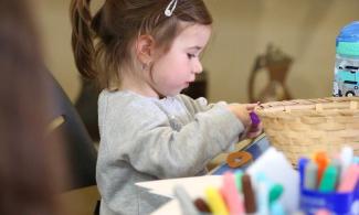 alt= "a young girl with long brown hair tied in a ponytail plays with arts and crafts supplies"
