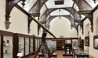 The Main Gallery in the Whipple Museum. Photo shows a large telescope, a Jacobean roof and display cases.