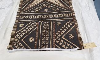 The short end of a long rectangular piece of barkcloth decorated with large zigzag motifs and four-pointed stars.