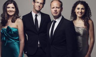 Two women dressed in satin dresses and two men in black suits, standing in a line and smiling.